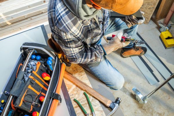 A construction worker sits on the floor, focused on using tools from a nearby toolbox during a home renovation, emphasizing craftsmanship and attention to detail.