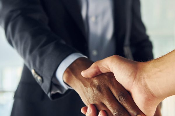 Doing handshake with customer. Young african american businessman in black suit is indoors.